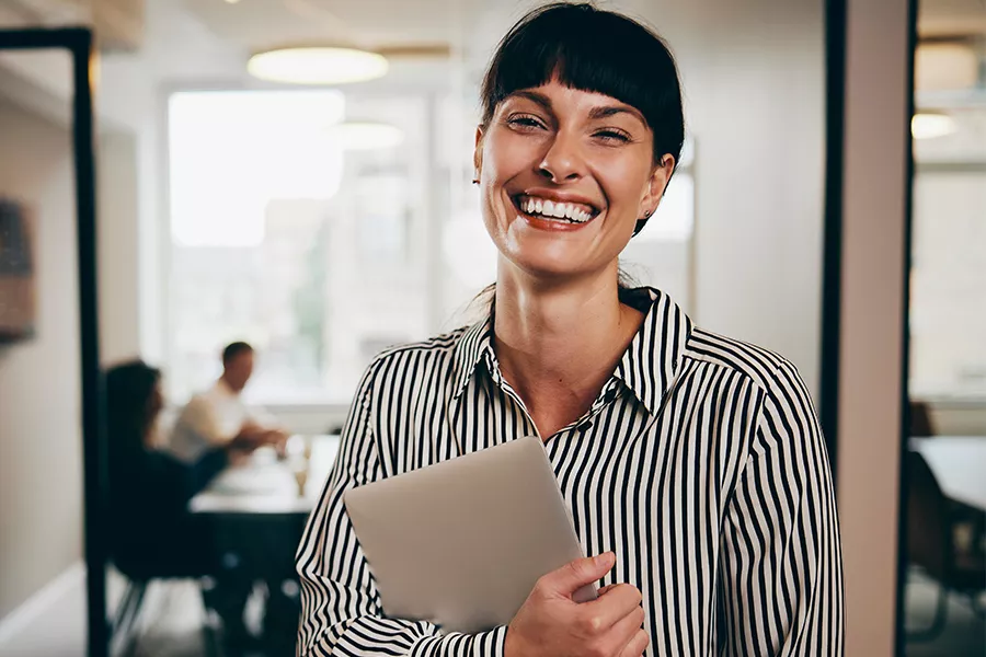 Collaboratrice Kelio souriante avec un ordinateur illustrant la gestion des compétences et des talents.