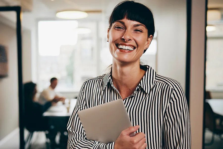 Collaboratrice Kelio souriante avec un ordinateur illustrant la gestion des compétences et des talents.